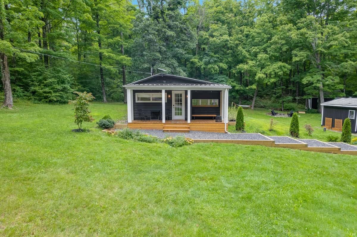 The cabin seen across the full width of the lawn, small against the tree line