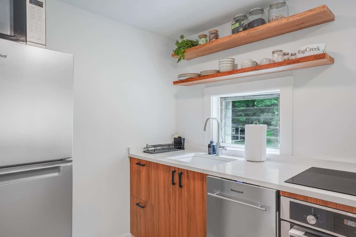 Open wood shelves above the kitchen window, with the sink, dishwasher, and cooktop below