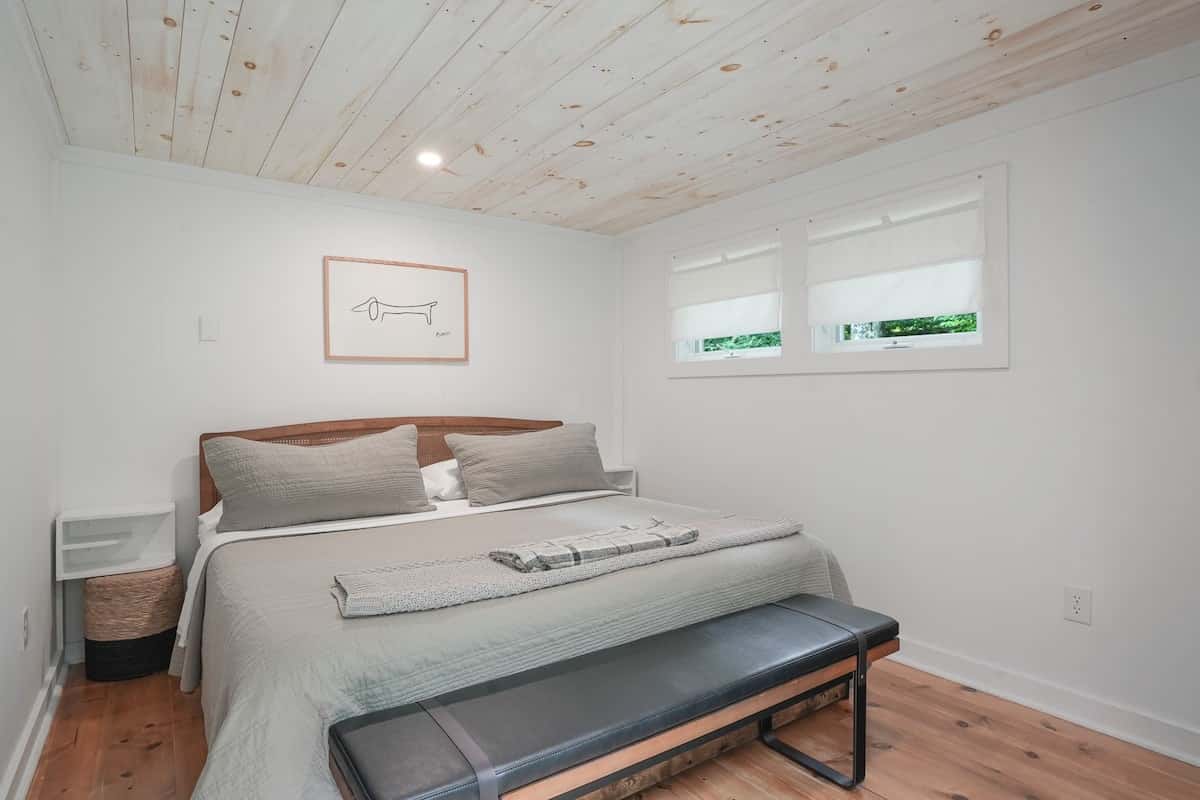 The bedroom: a king bed under a whitewashed pine ceiling, with a bench at the foot of the bed
